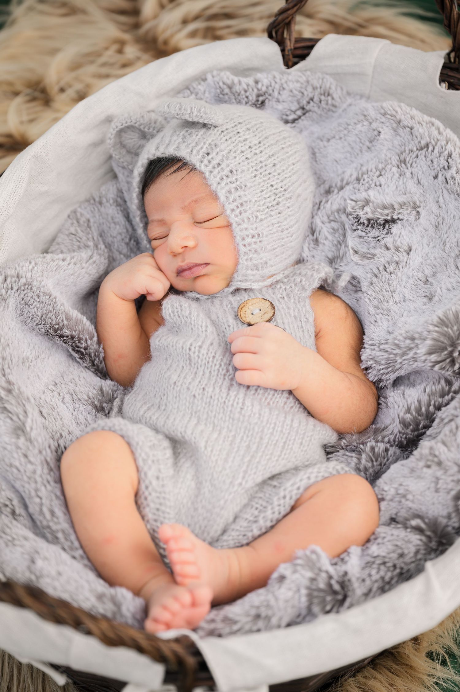 A sleeping newborn wrapped in soft gray knit blankets during a professional photography session.