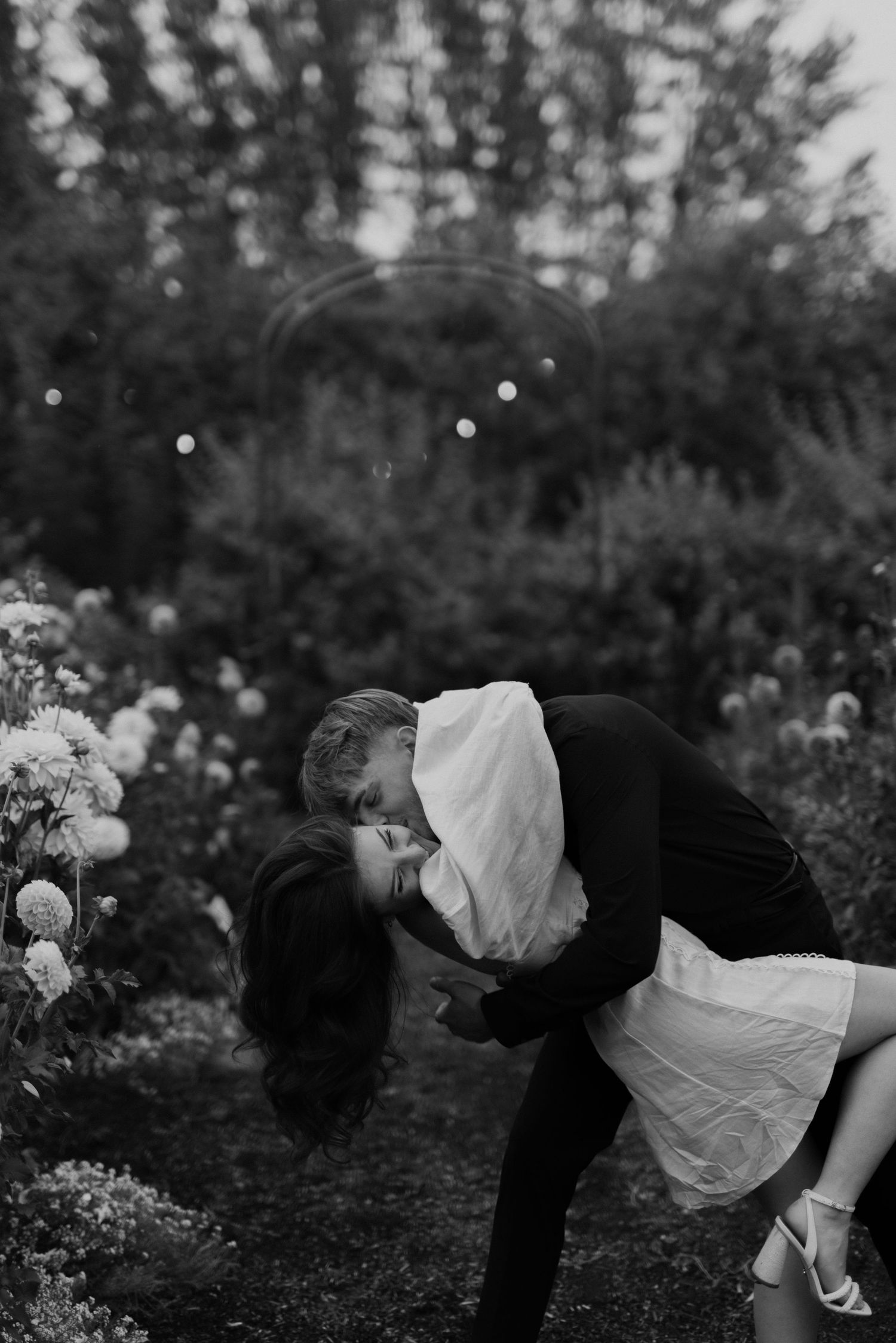 Black and white romantic shot of couple dip and kissing in a flower garden