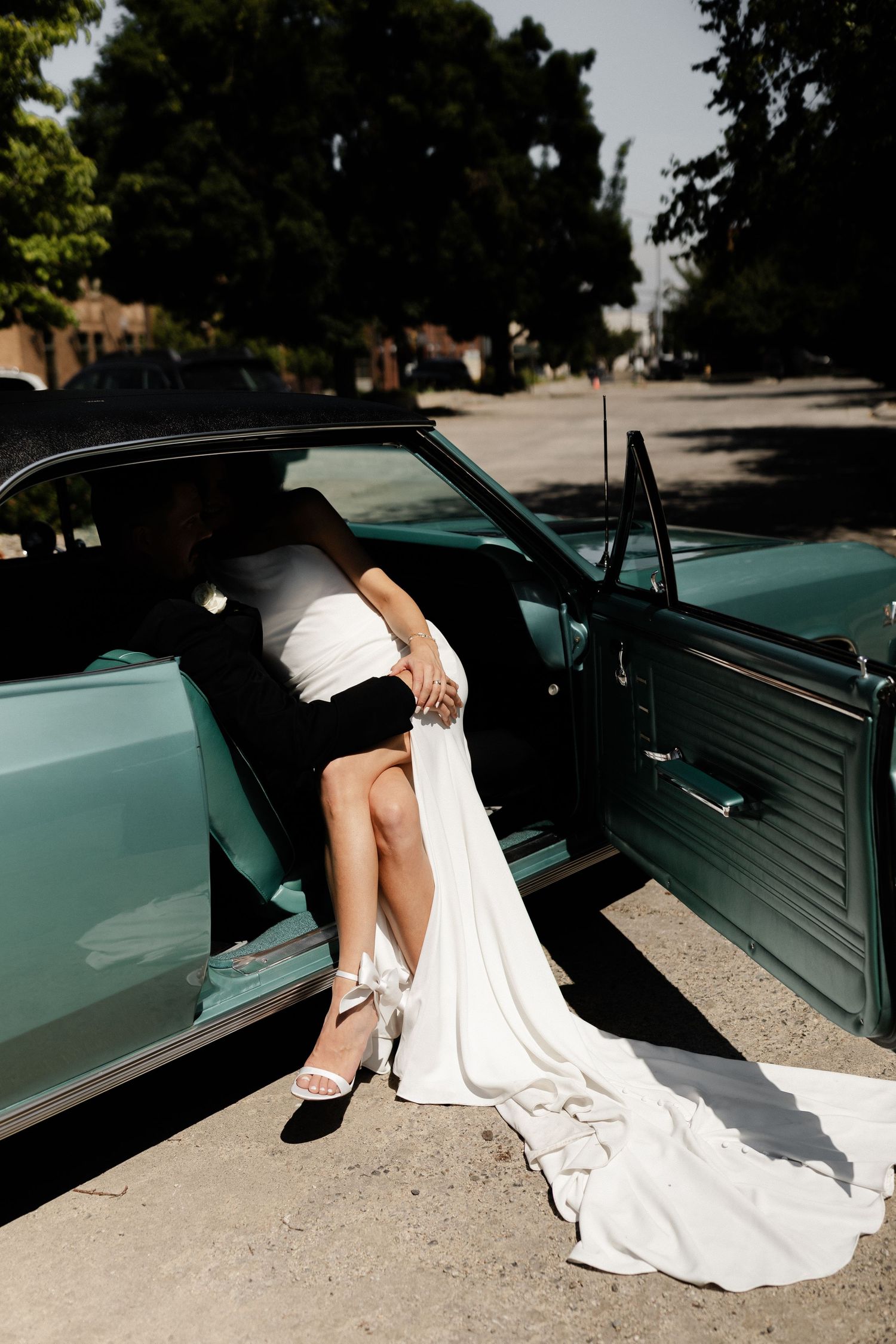 artistic photo bride and groom sitting in 1970 classic chevelle in direct sunlight