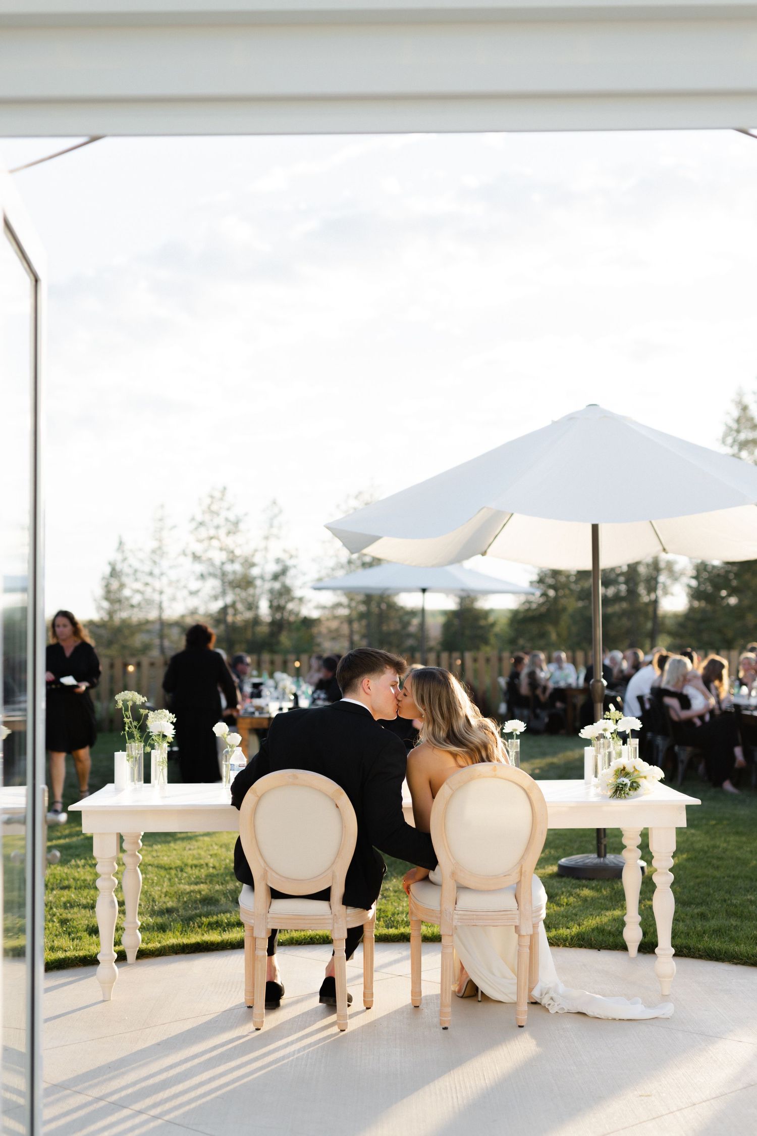 Bride and groom kissing at their sweetheart table with an umbrella over the table