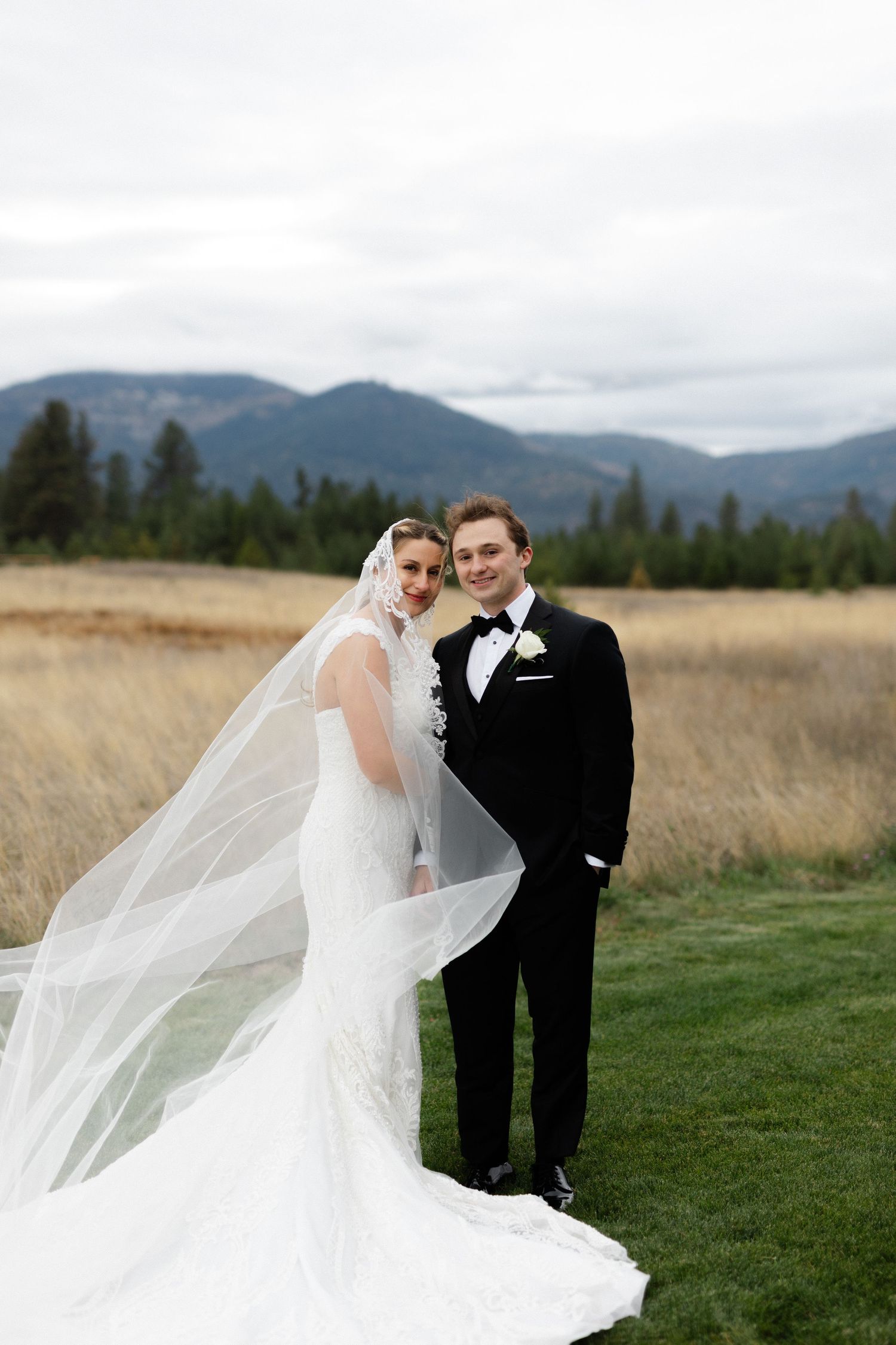 Couple looking at the camera with a mountain background, wind blowing brides cathedral veil.