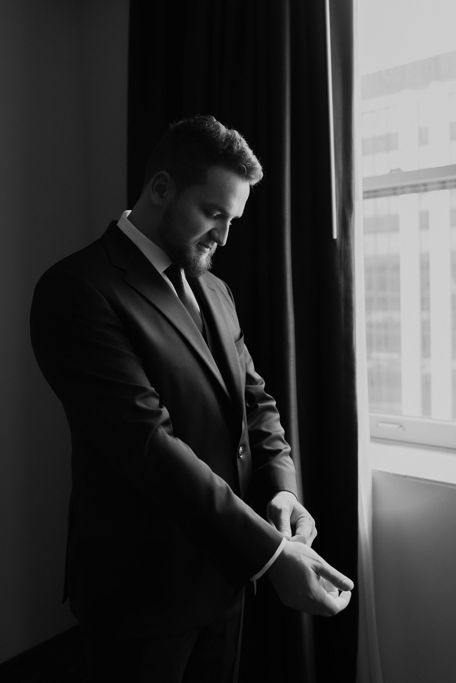 artisitc light photo of groom fixing his cuffings