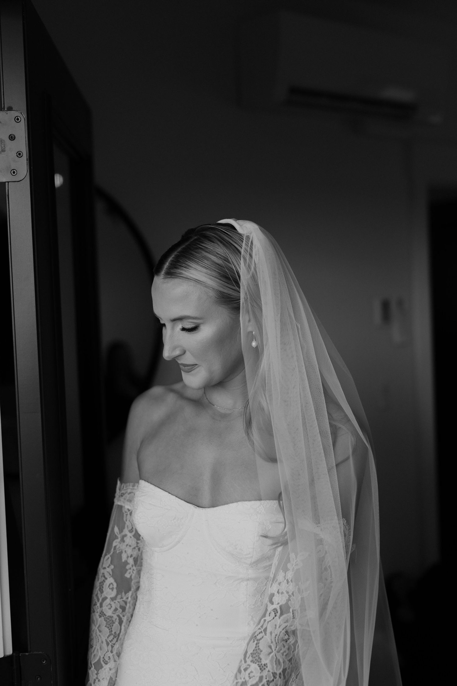 black and white portrait of bride with lacy dress, gloves, and veil on looking down. Greenhouse on greenbluff