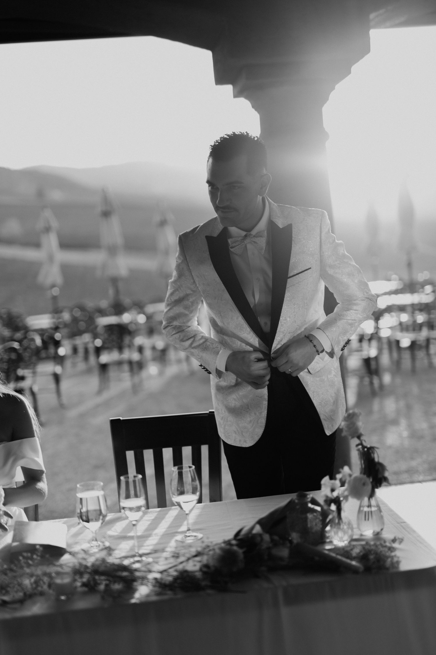 groom buttoning his jacket on wedding day with sun flare shooting in the camera