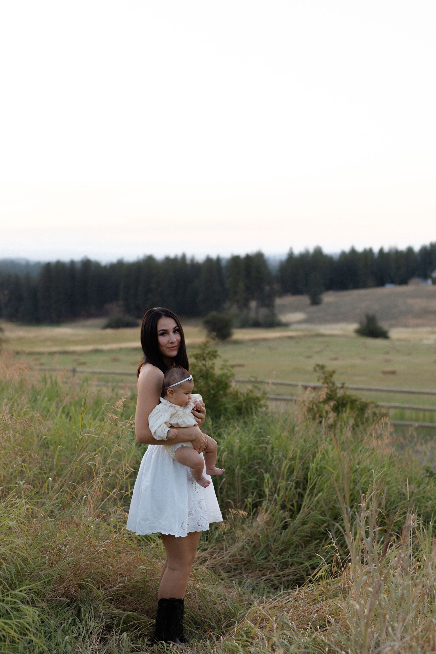 woman standing in a countryside road with a field view holding her baby