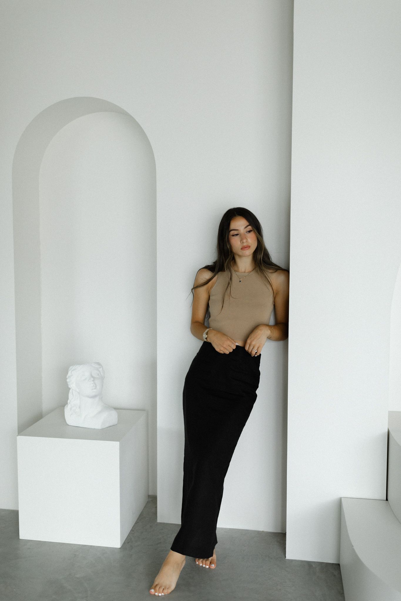 woman stylishly dressed leans against a wall in a studio