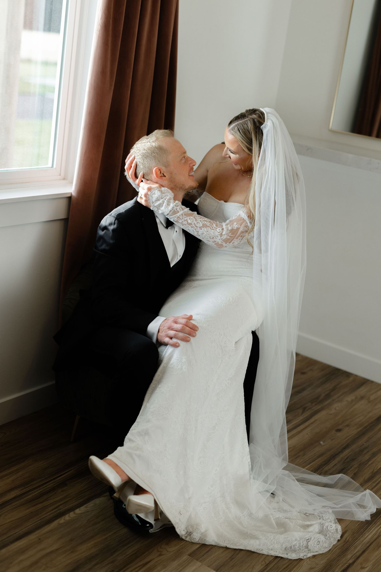Bride sitting on grooms lap ,hugging him in the bridal suite