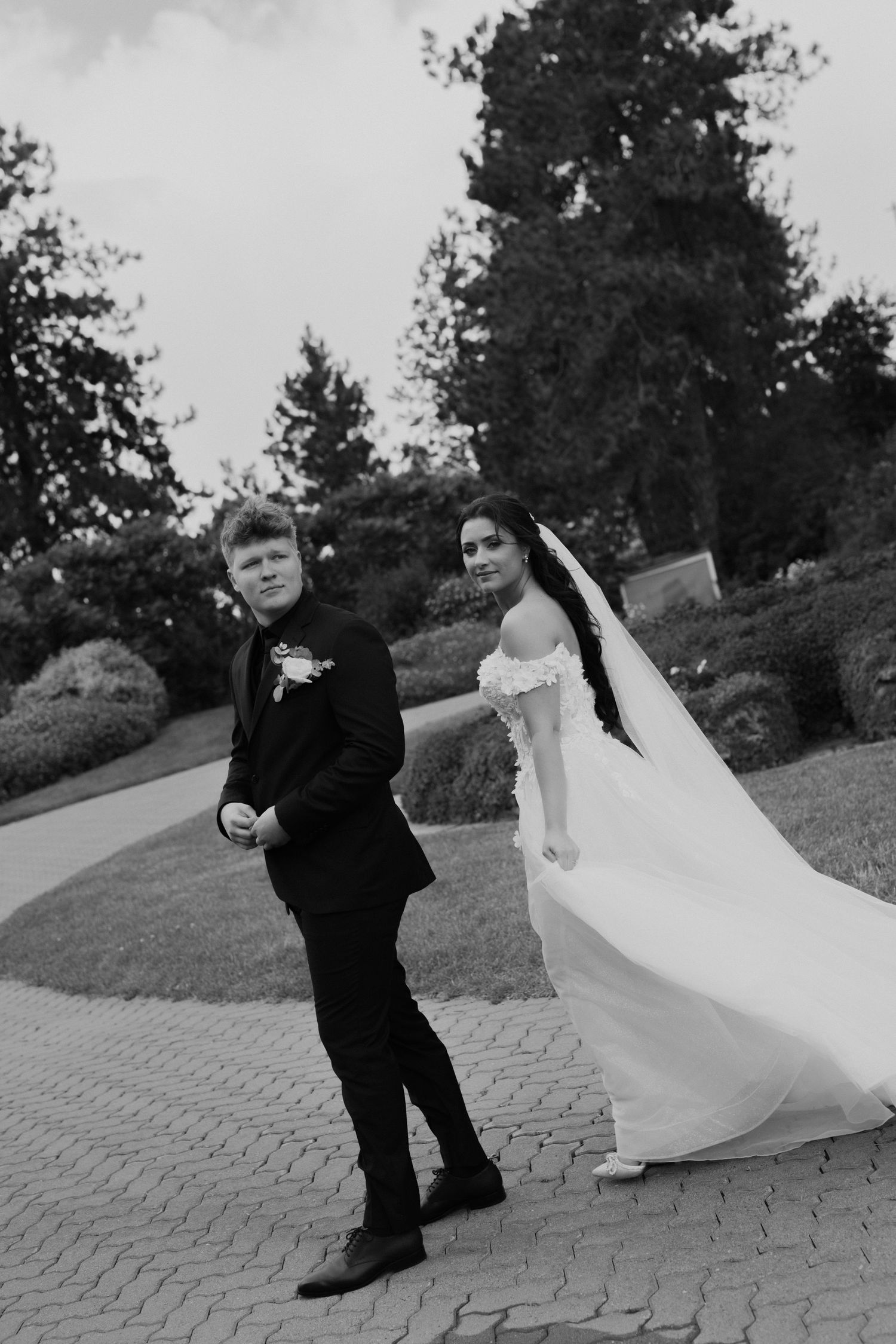 Black and white tilted photo of bride and groom looking back with wind blowing