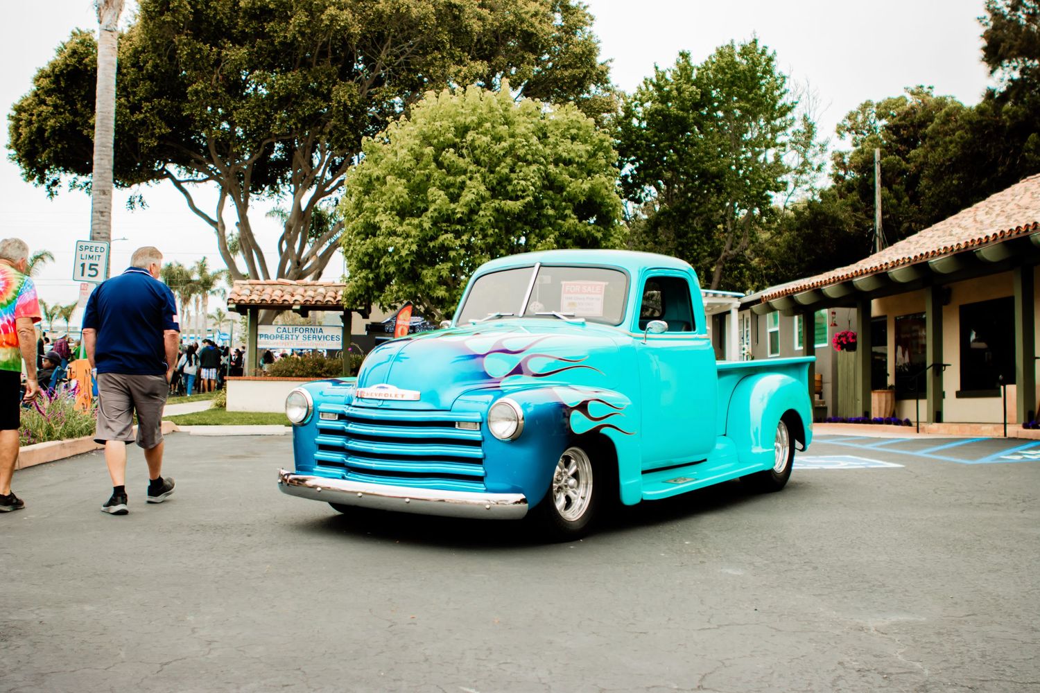A bright turquoise vintage Chevrolet pickup truck parked on a street near some buildings and trees.