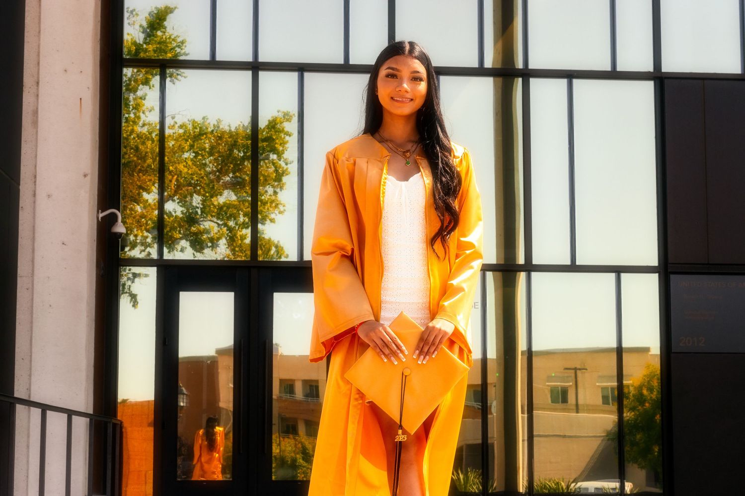 A person in a bright orange pantsuit poses elegantly in front of geometric black and white window panes on a sunny day.