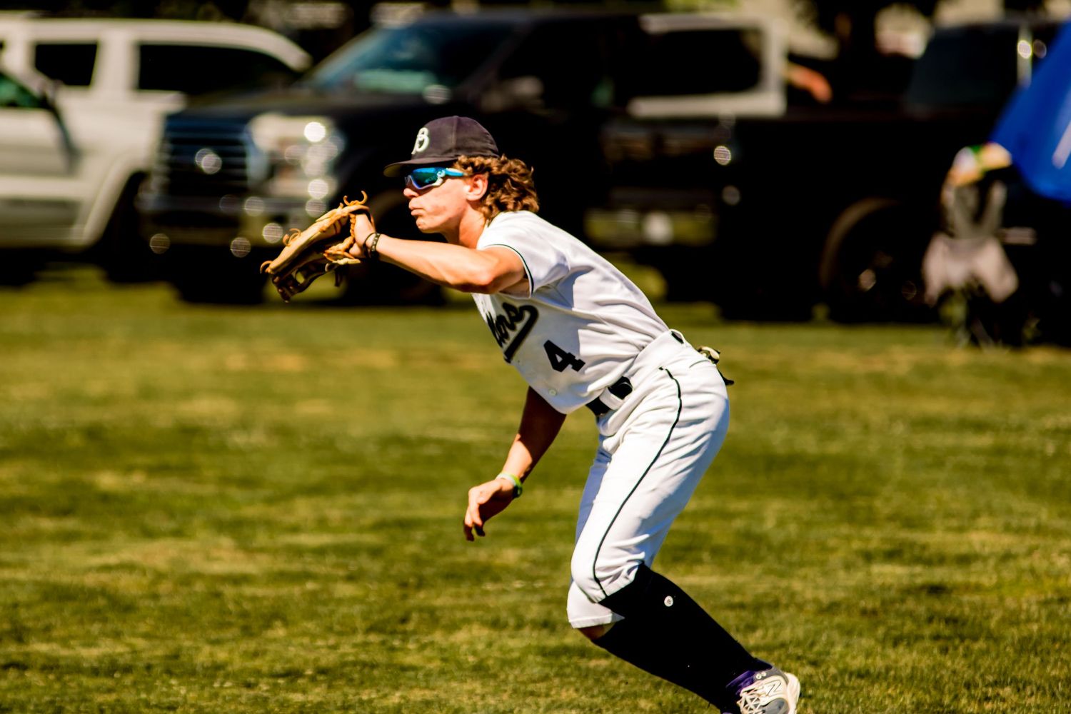 Baseball player in white uniform ready in fielding stance during daytime game on grass field.
