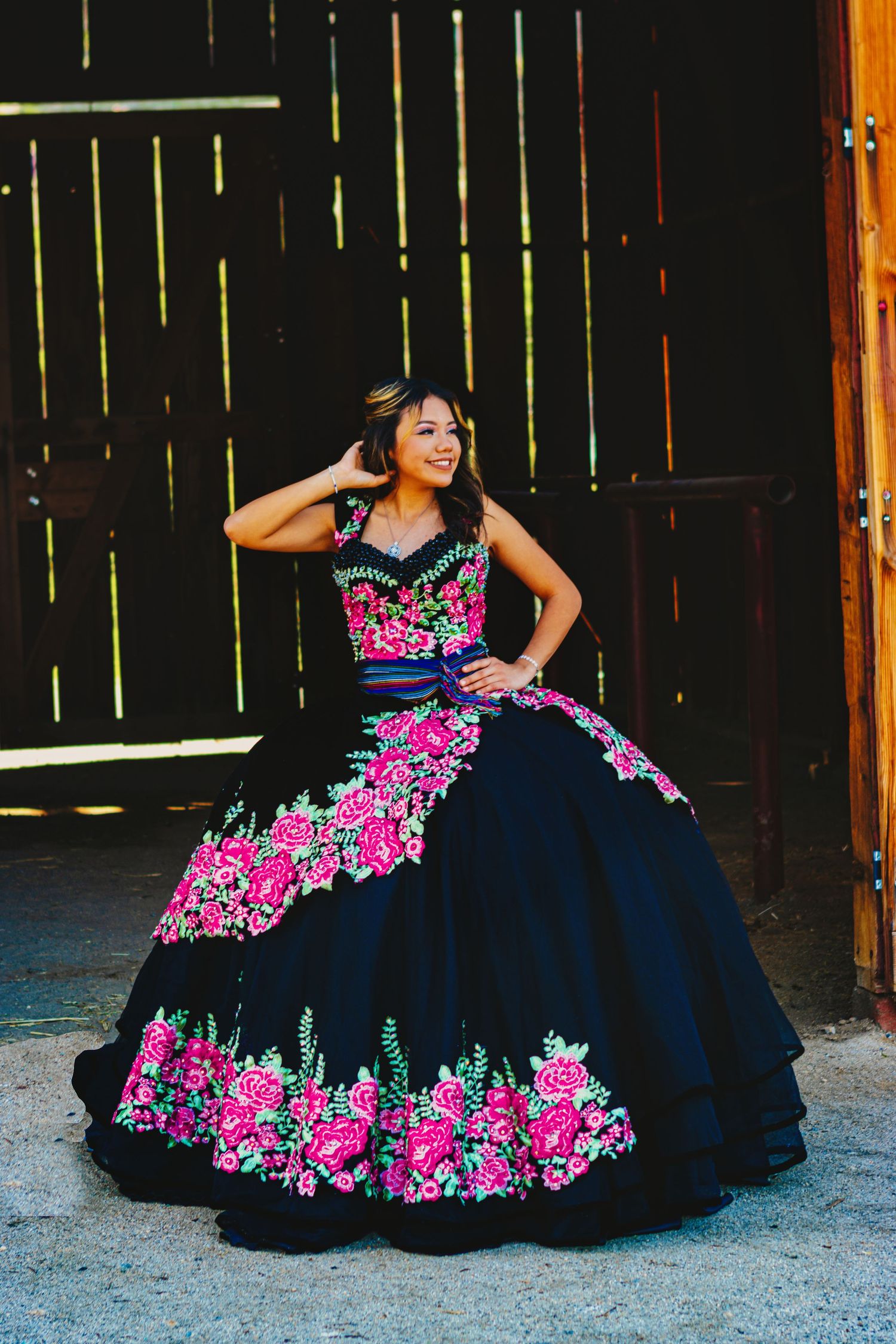 A stunning navy blue quinceañera dress adorned with vibrant pink floral embroidery in a rustic barn setting.