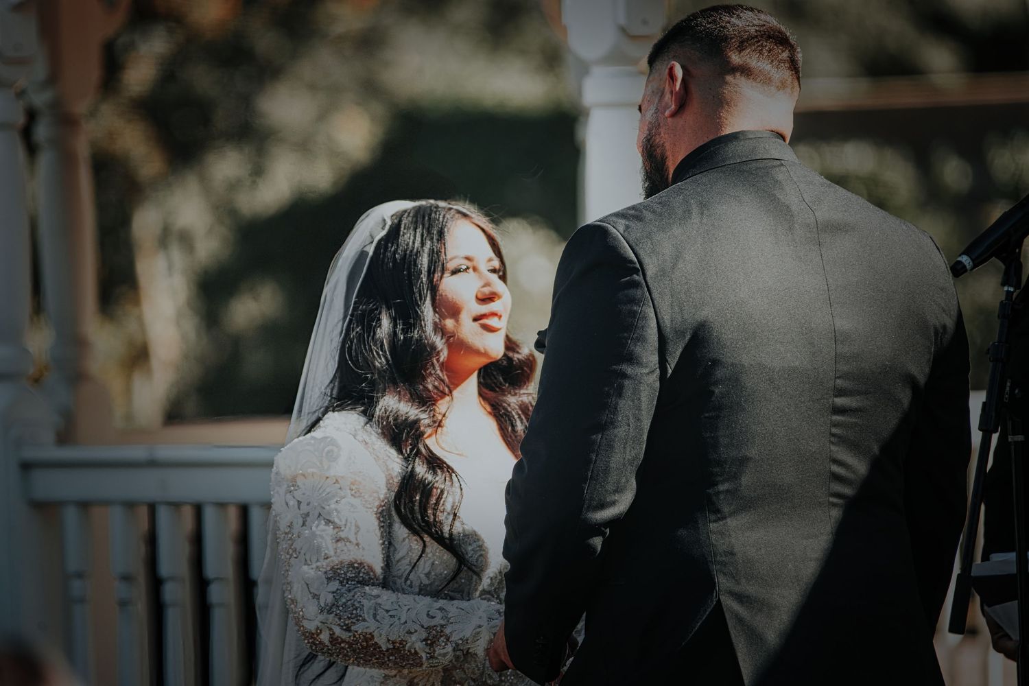 A bride in a lace dress laughs joyfully during an outdoor wedding ceremony on a porch.