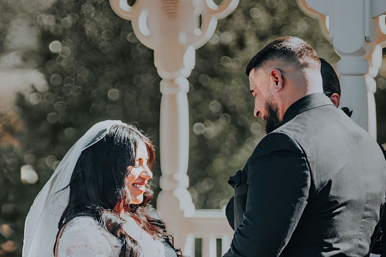 A couple shares a joyful moment together during their outdoor wedding ceremony near a decorative white pillar.