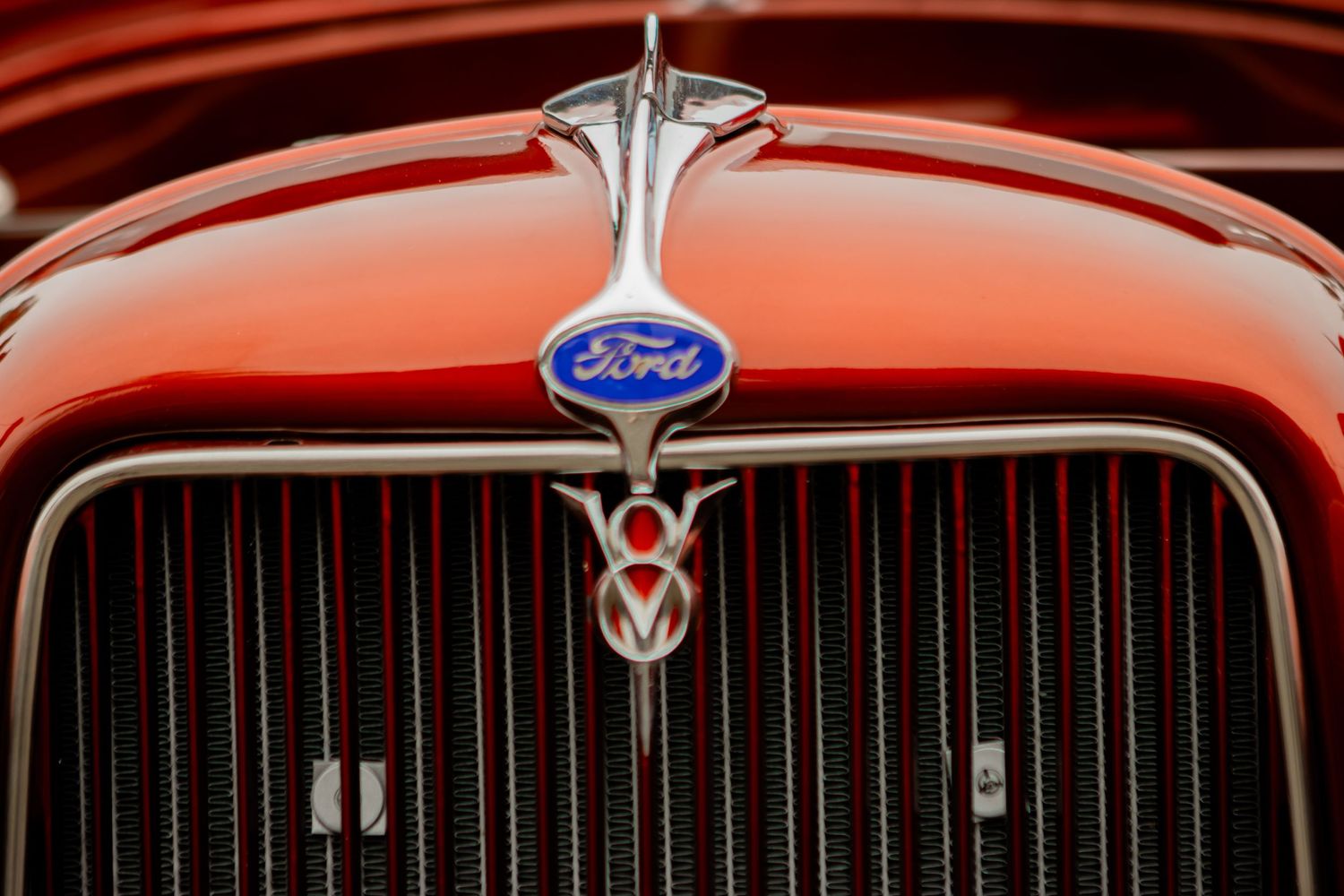Close-up view of a vintage Ford V8 emblem and vertical grille on an orange-colored classic car.