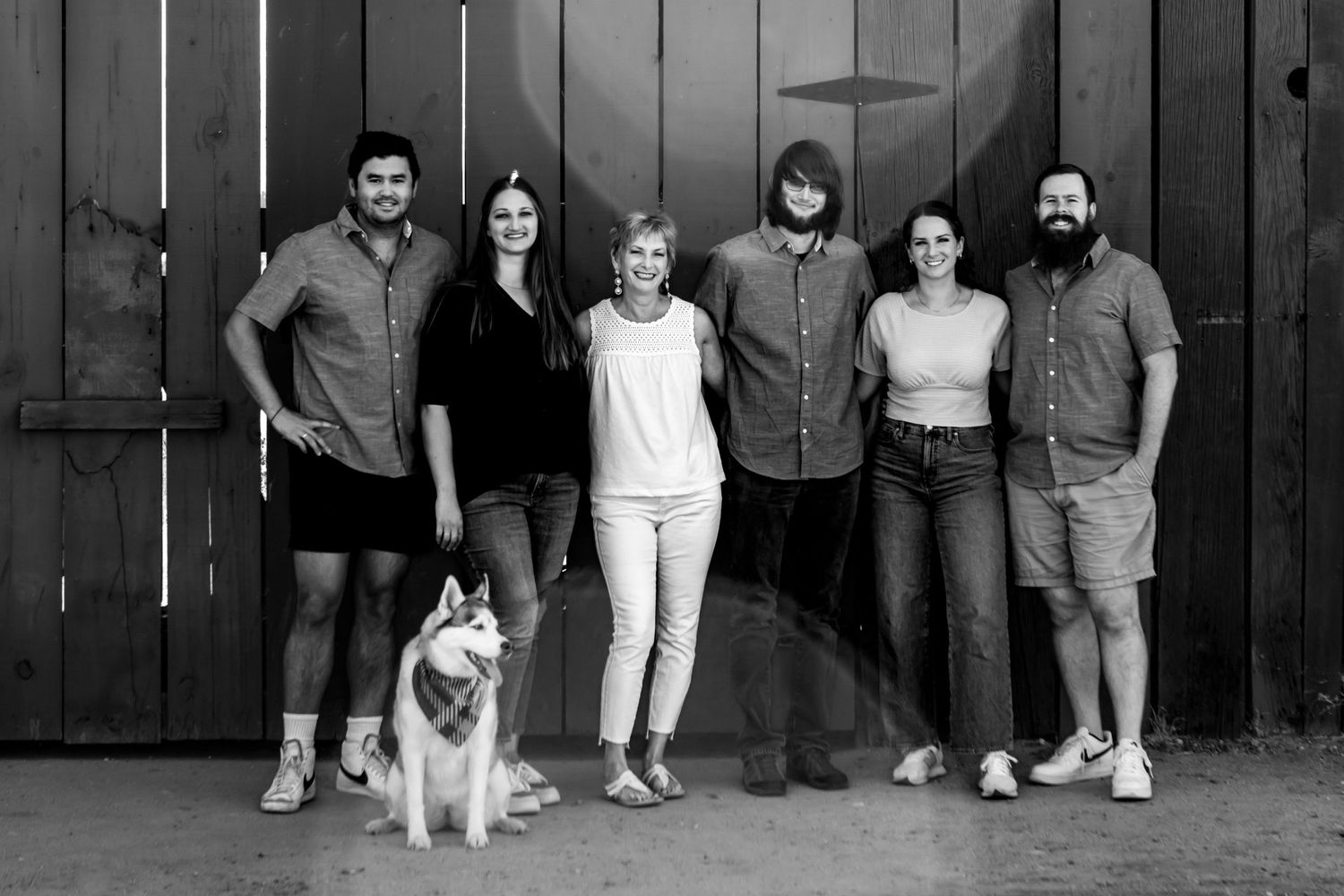 Black and white group portrait with a husky dog against a wooden wall backdrop.