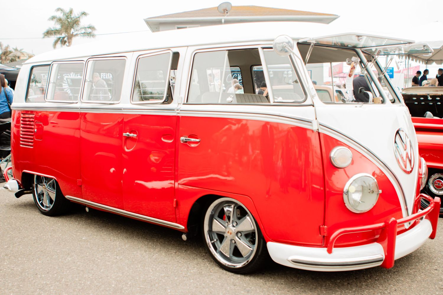 Classic red and white Volkswagen Type 2 bus with custom wheels parked at an outdoor event.
