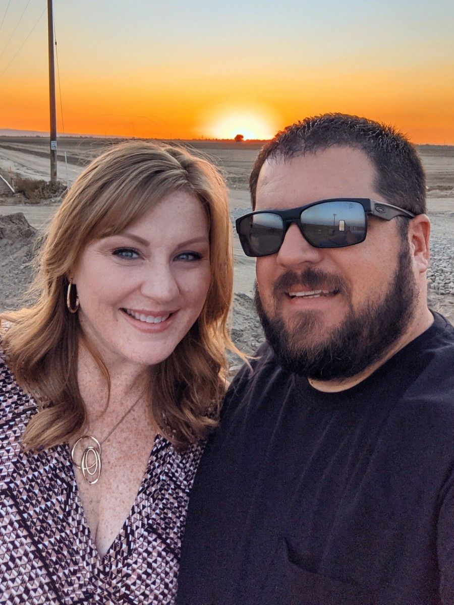 Two people take a selfie together against a vibrant orange desert sunset backdrop.