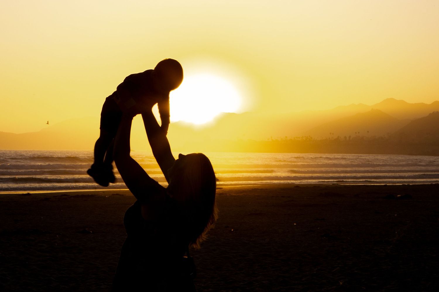 Silhouettes of two people playing on a beach at sunset create a heartwarming scene against an orange sky.