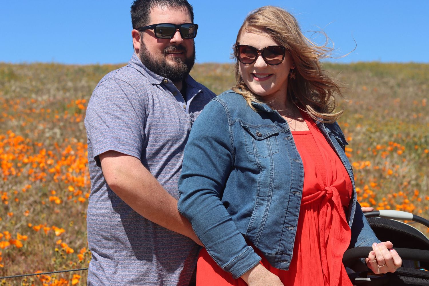 Couple poses together in a field of blooming orange poppies on a sunny spring day.