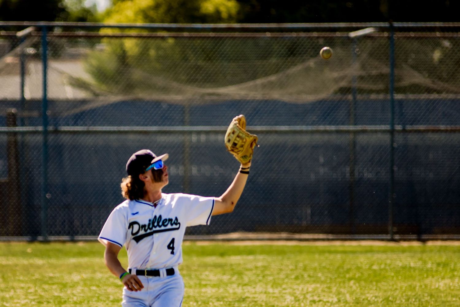 Baseball player reaching up to catch a ball on a sunny day at a baseball field.