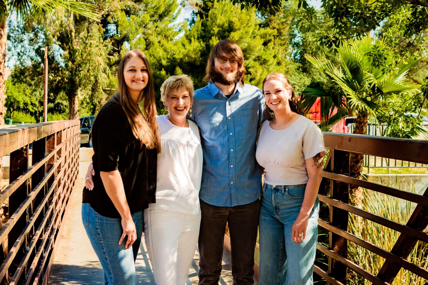 Group of four people smiling on wooden bridge with lush greenery in background.