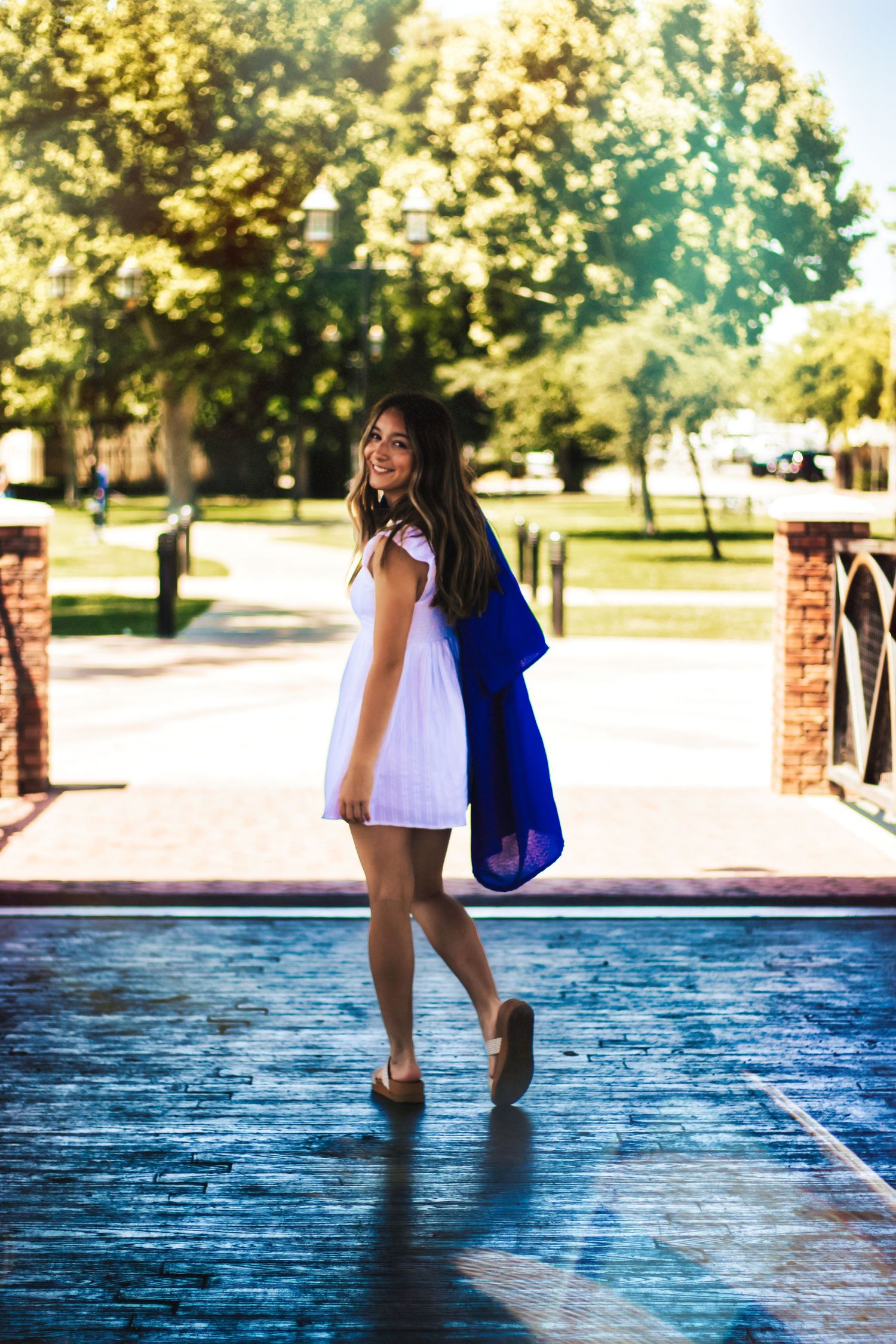 A person in a white dress and blue robe walks along a wet pathway on a sunny summer day.