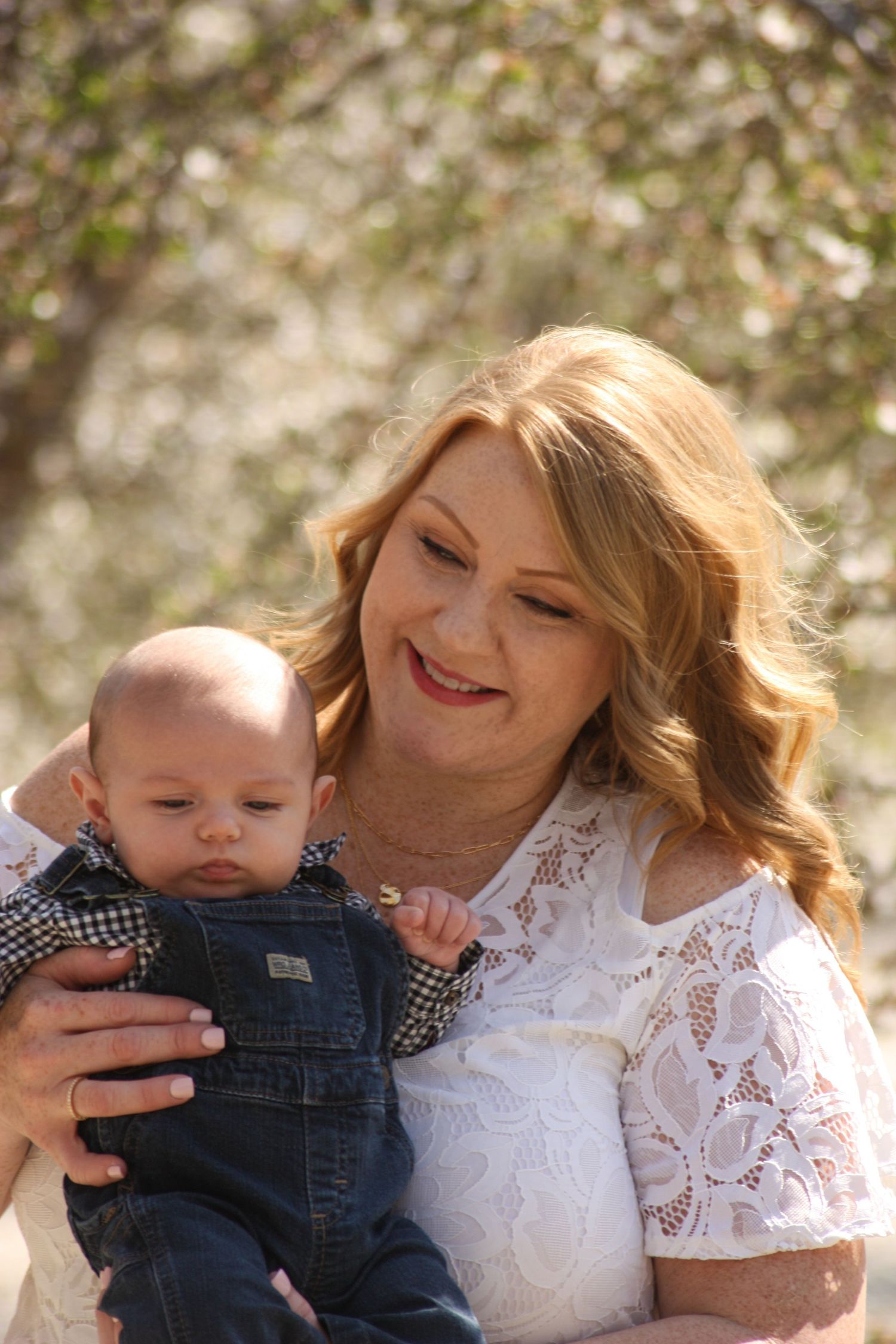 A tender moment between parent and baby in white lace dress against blooming trees.