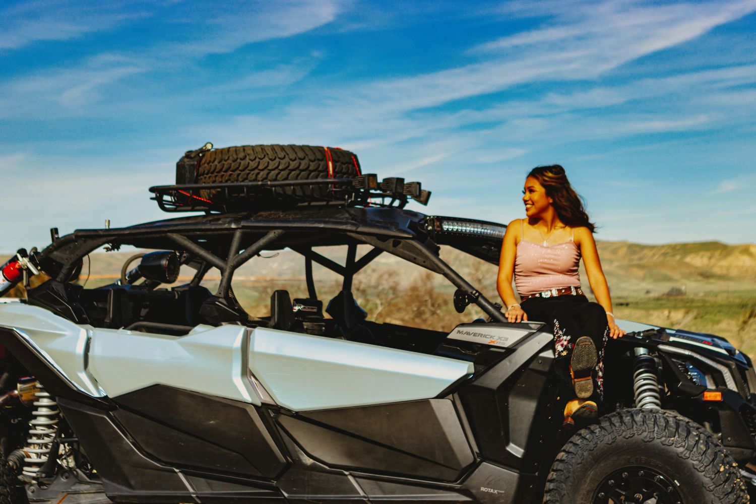 Off-road vehicle with roof rack parked in desert landscape under blue sky with wispy clouds.