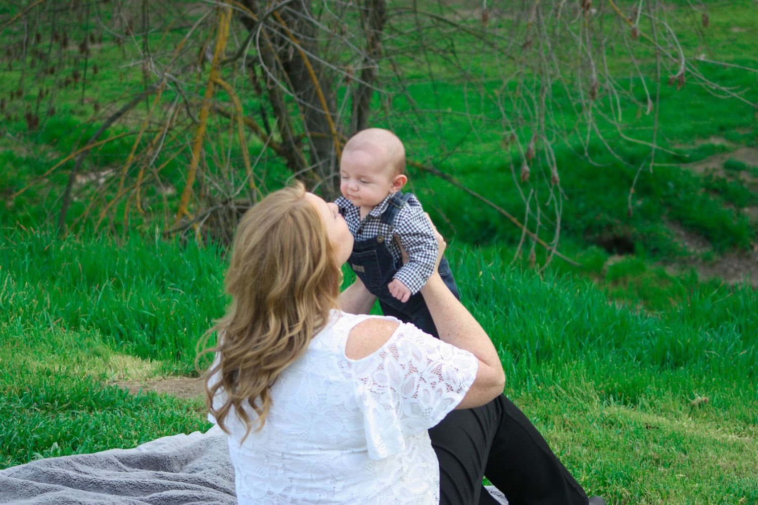 Mother and baby sharing playful moment on blanket in green spring meadow.