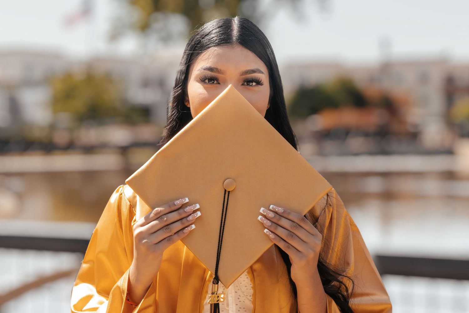 A graduate in a bright yellow academic gown holds their diploma up to cover their face during a graduation ceremony.