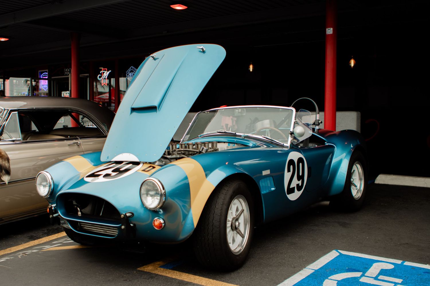 A classic blue and yellow Cobra racing car with number 29 displayed at a vintage car show with its hood up.