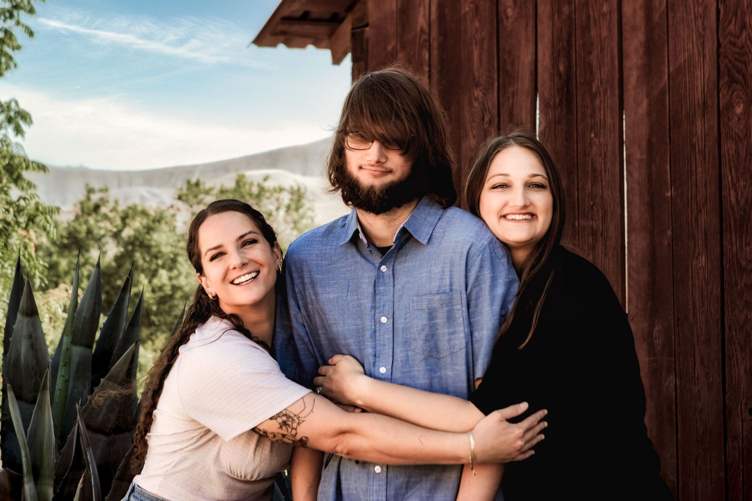 Small group embracing and smiling in front of a rustic red barn.