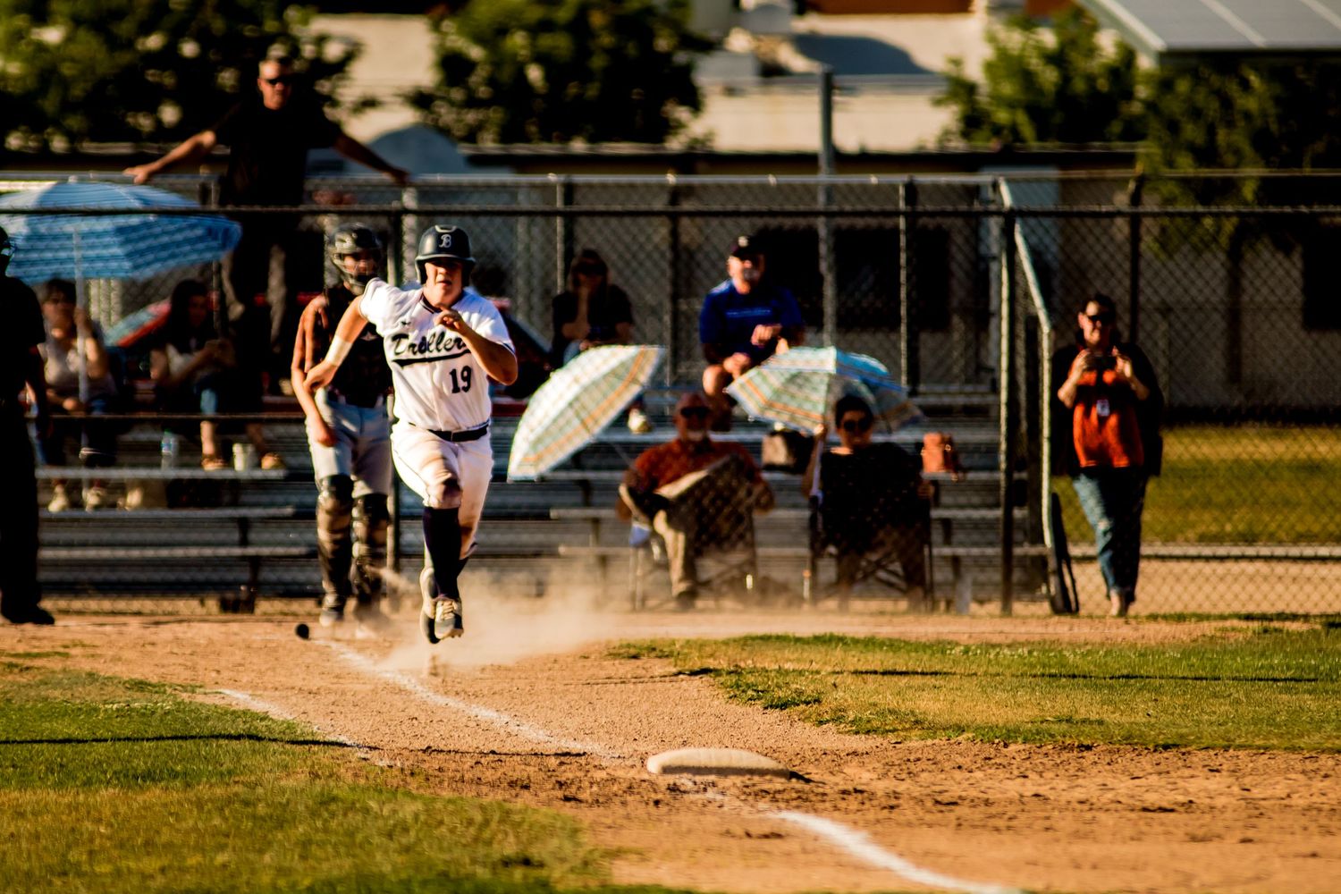 Baseball player sprinting toward first base during a sunset game on a dirt infield.