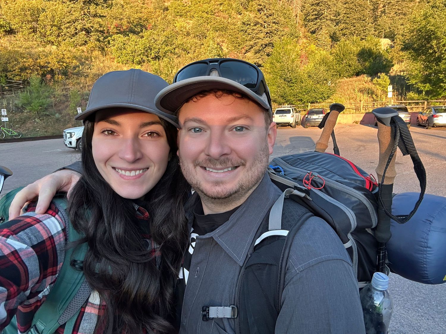 Couple smiling together at camera wearing hiking backpacks and gear getting ready to hike a mountain for website Boudoir by Bri Saint Louis