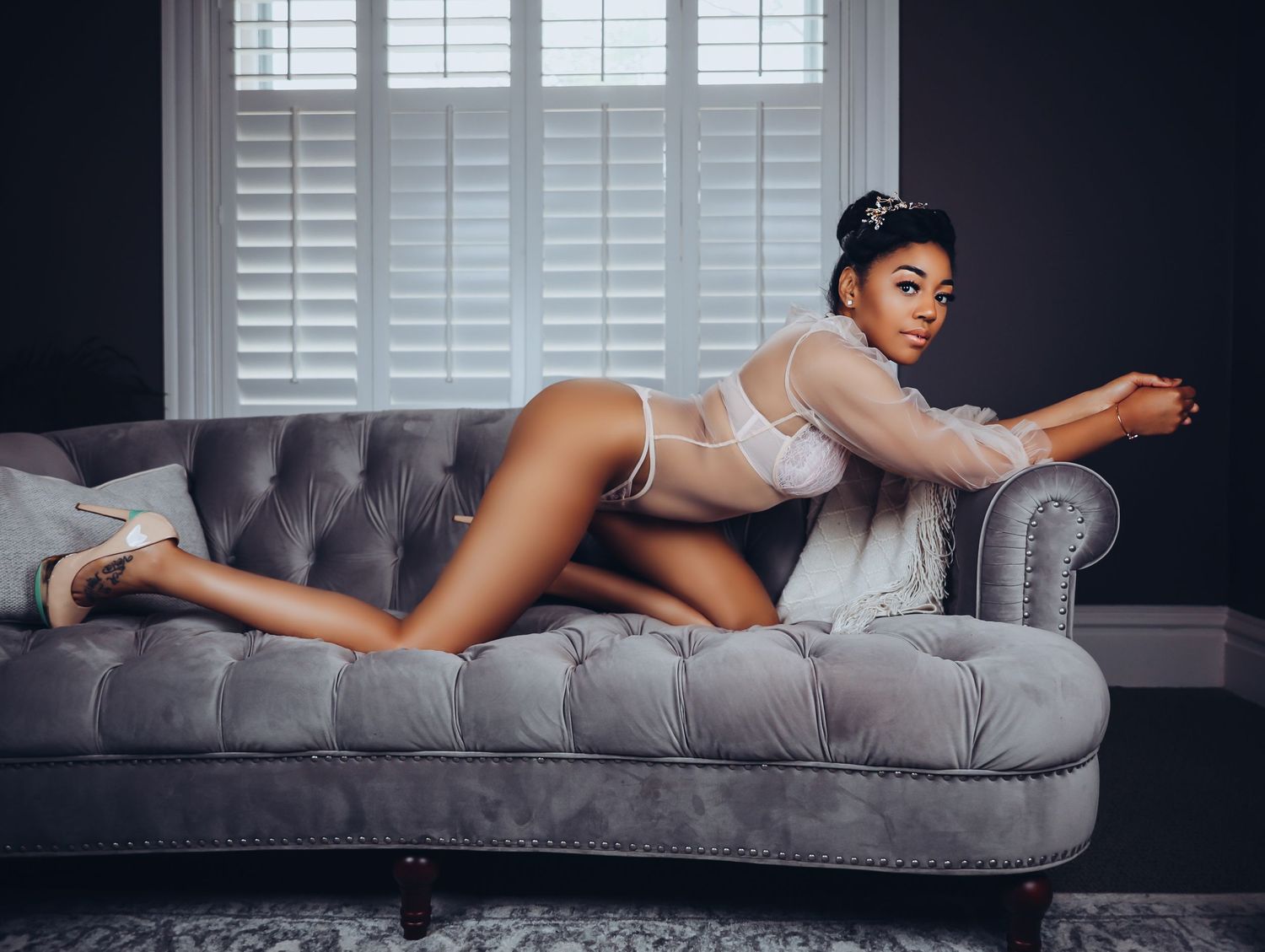 Beautiful woman draped across gray velvet couch posing in pink lingerie for photoshoot with Boudoir by Bri Saint Louis