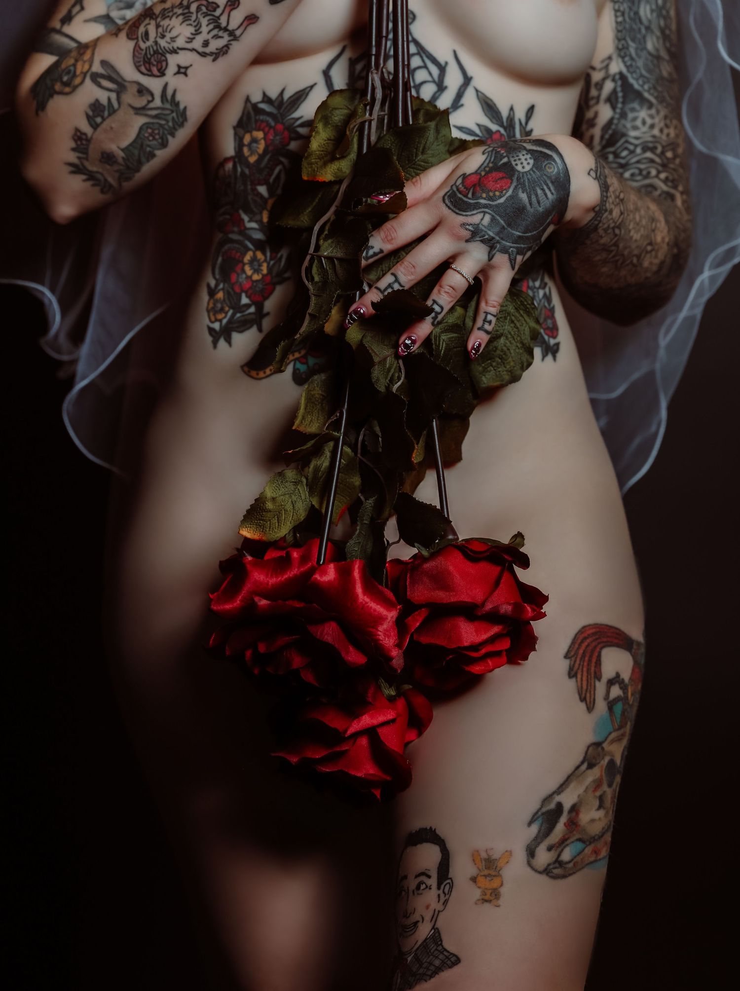 Cropped image of pale, tattooed woman wearing bridal veil and holding long-stemmed roses for photoshoot with Boudoir by Bri in Saint Louis