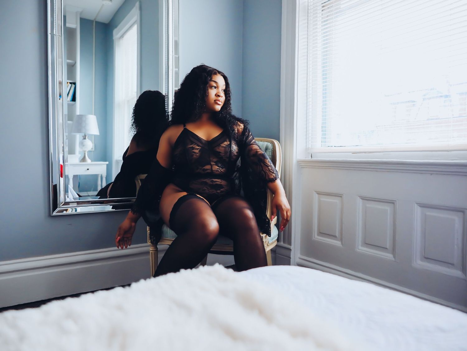 Beautiful woman sitting in vintage chair in bedroom looking out window in black lingerie set and stockings for Boudoir by Bri in Saint Louis