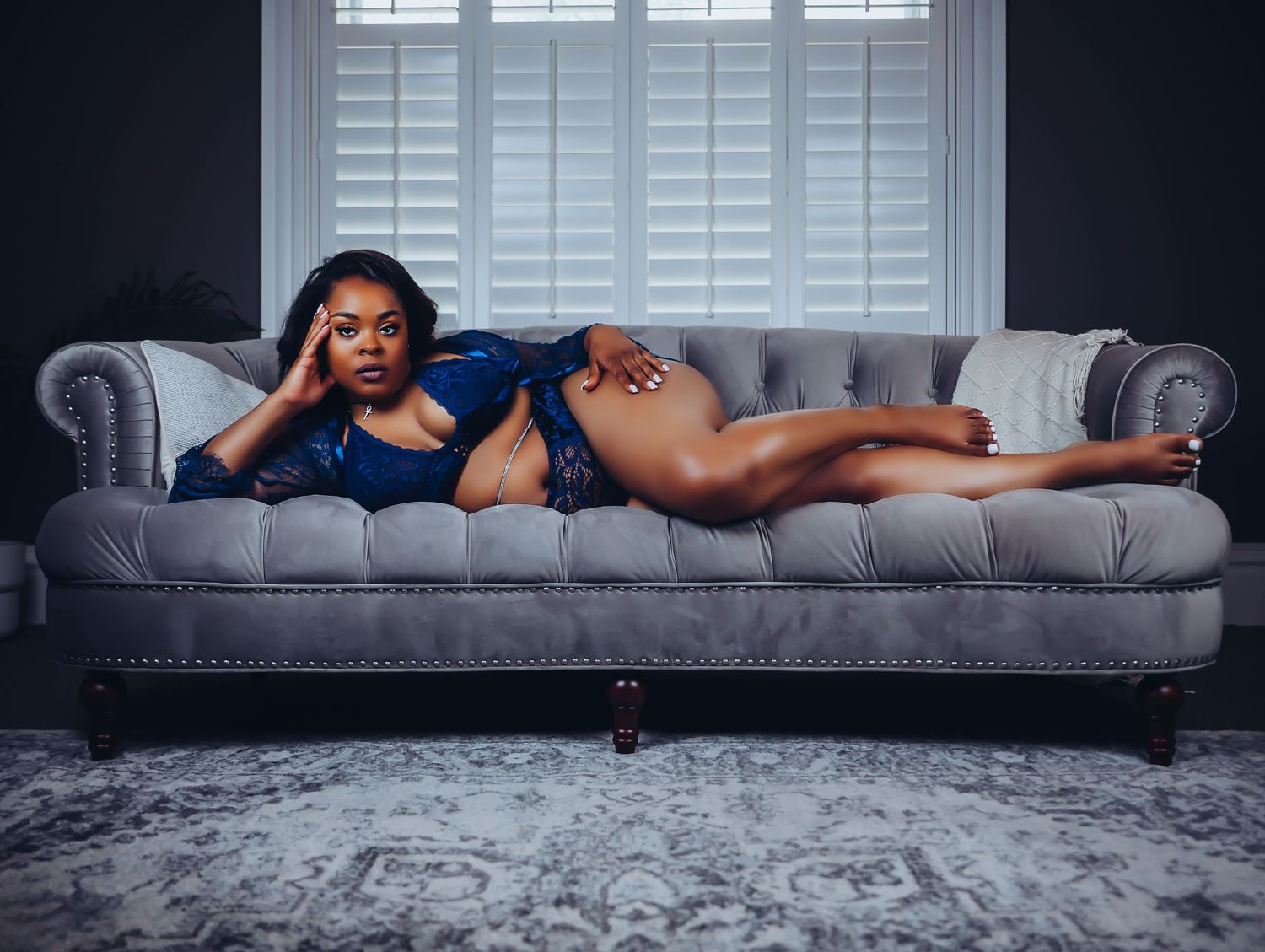 Beautiful woman draped across gray velvet couch posing in blue lingerie for photoshoot with Boudoir by Bri Saint Louis