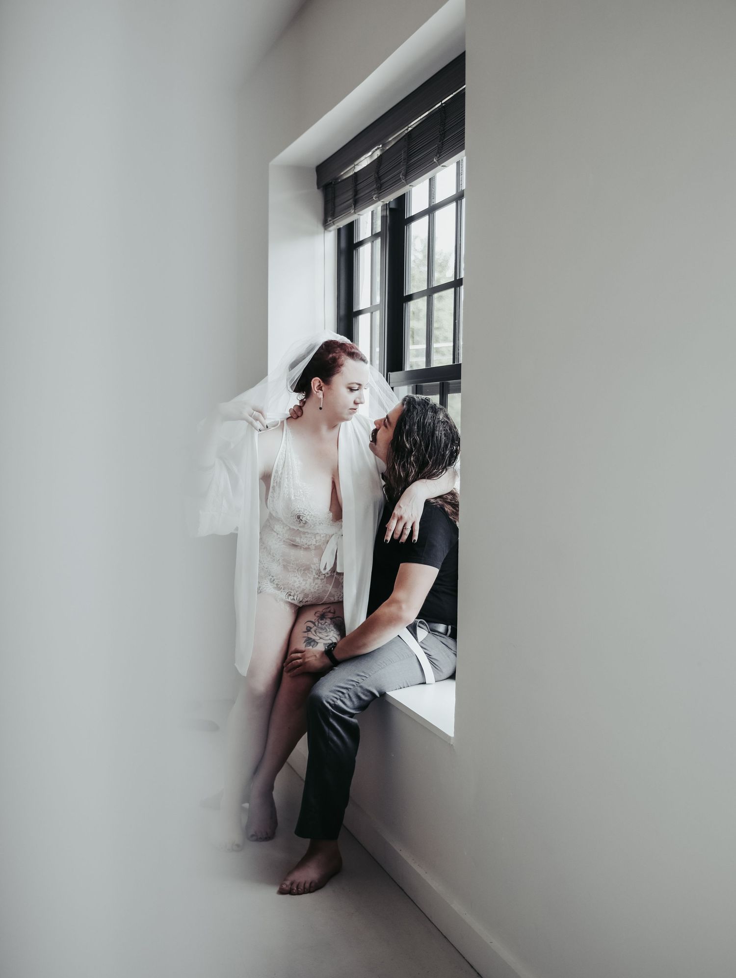 Boudoir portrait bride and groom couple in love posing by window in white lingerie and veil for photoshoot with Boudoir by Bri Saint Louis