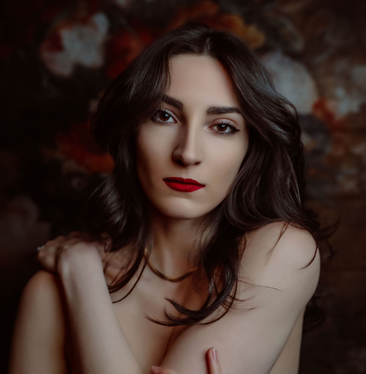 Dramatic headshot of pale woman with long black hair and red lipstick crossing arm over chest and looking into camera for Boudoir by Bri