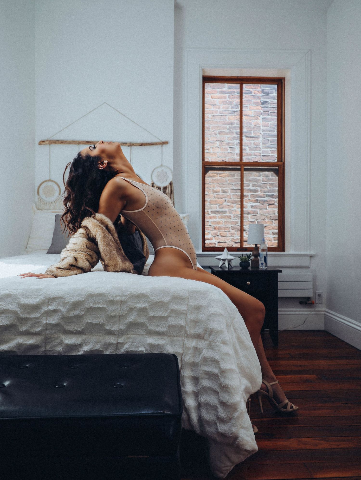 Beautiful woman in sheer bodysuit posing with fur coat for photoshoot with Boudoir by Bri Saint Louis white bedroom