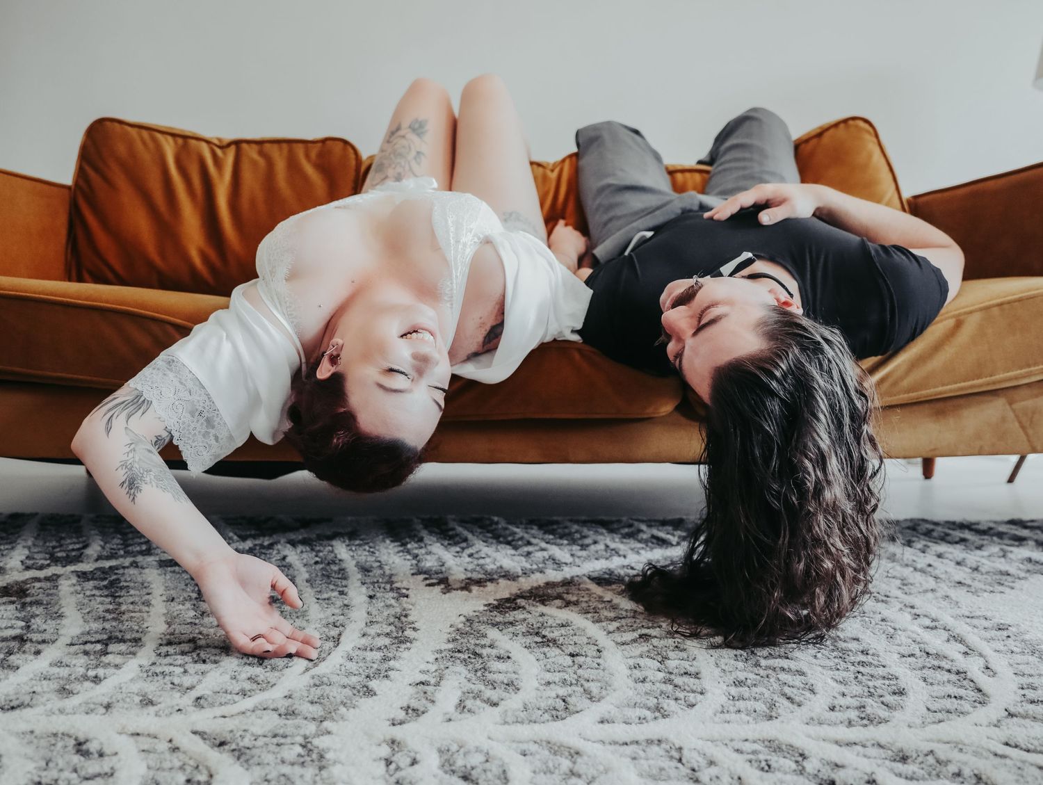 Young happy couple in love upside down laughing on orange couch for photoshoot session with Boudoir by Bri in Saint Louis
