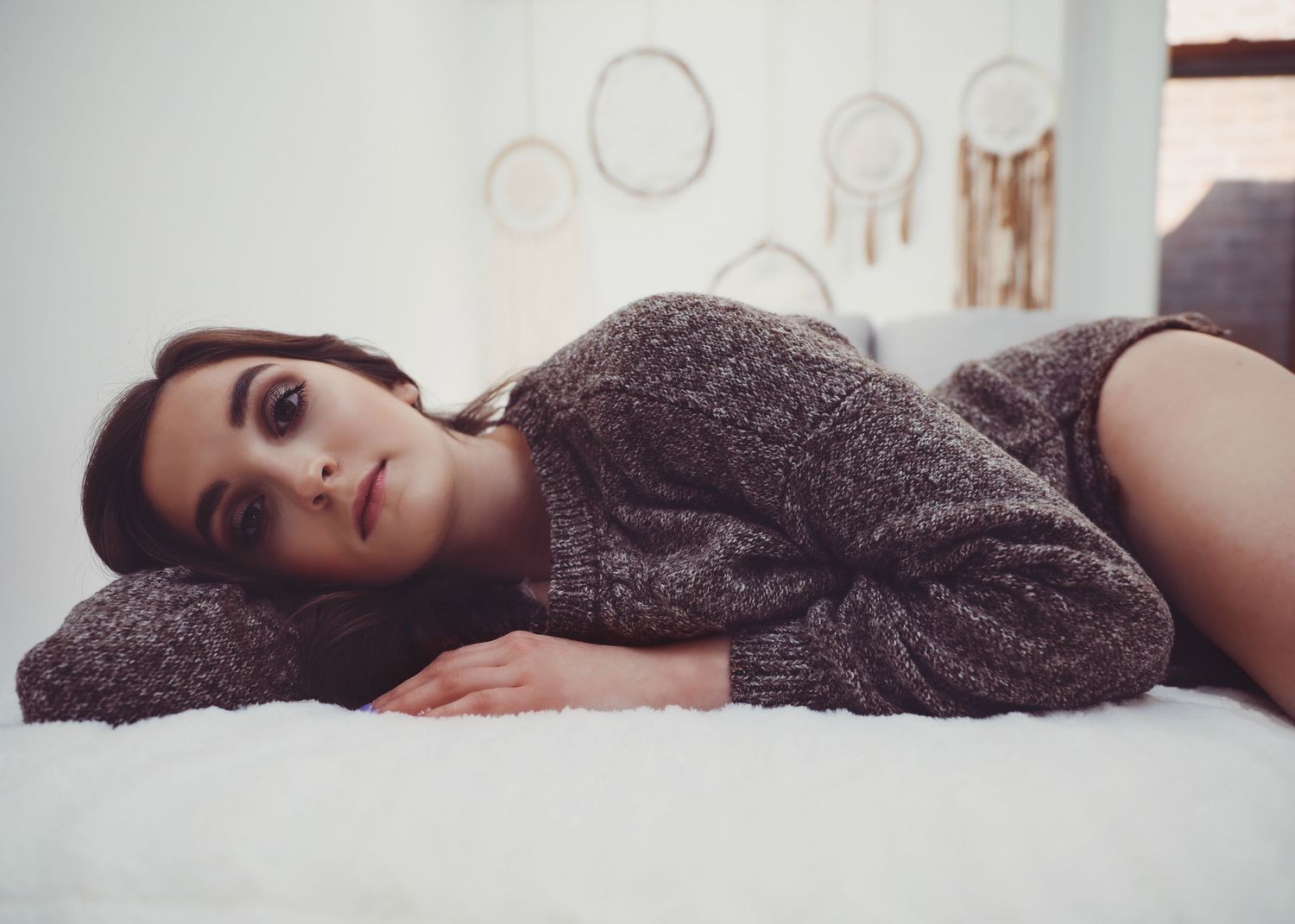 Boudoir portrait of beautiful young woman laying on side in cozy sweatshirt in white bedroom for photoshoot with Boudoir by Bri Saint Louis