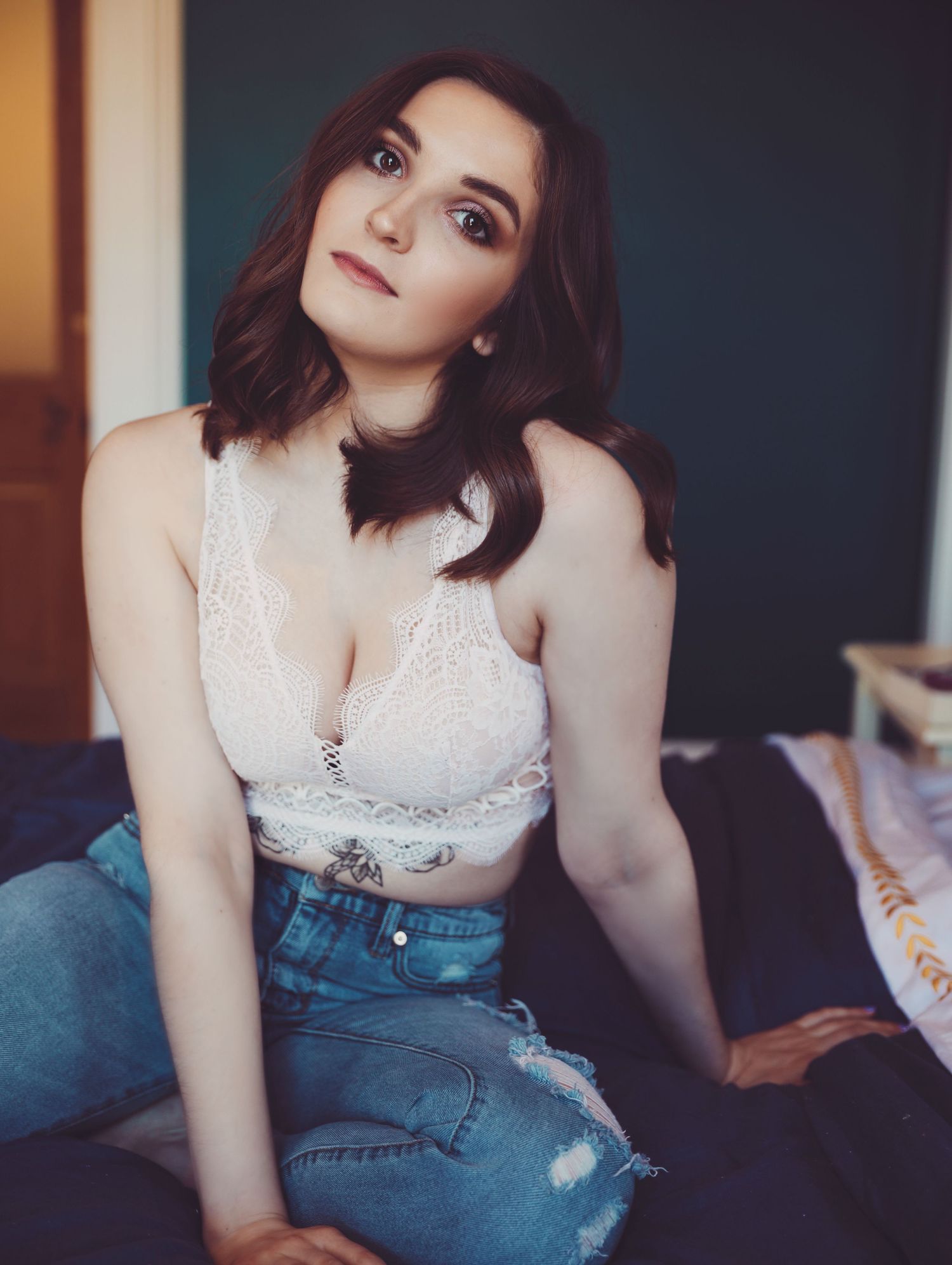 Boudoir portrait of beautiful young woman in white bra top and jeans posing in cozy blue bedroom photoshoot with Boudoir by Bri St. Louis