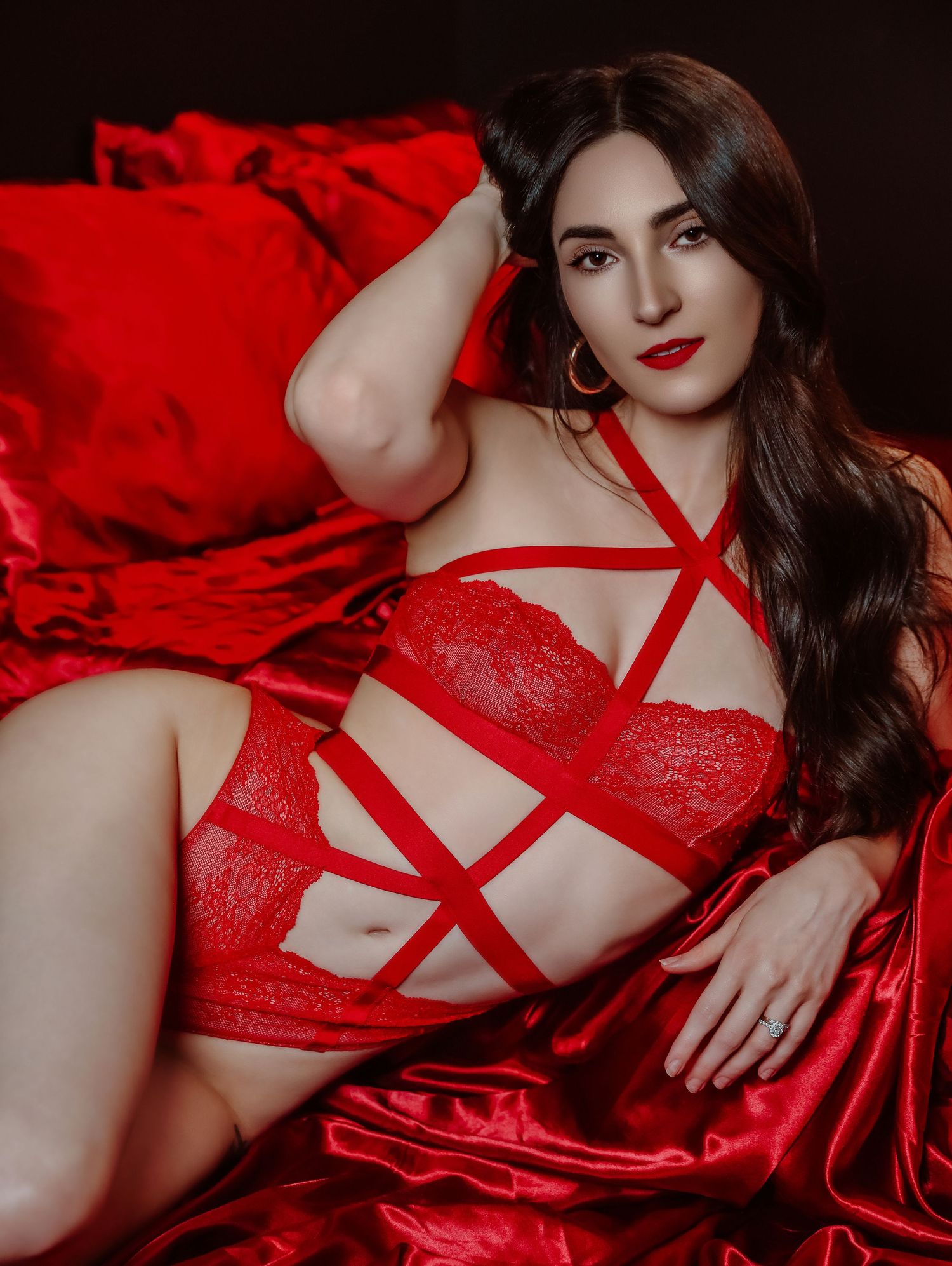 Young woman with long black hair posing in red scrappy lingerie on red satin bedsheets and red lipstick for Boudoir by Bri Saint Louis