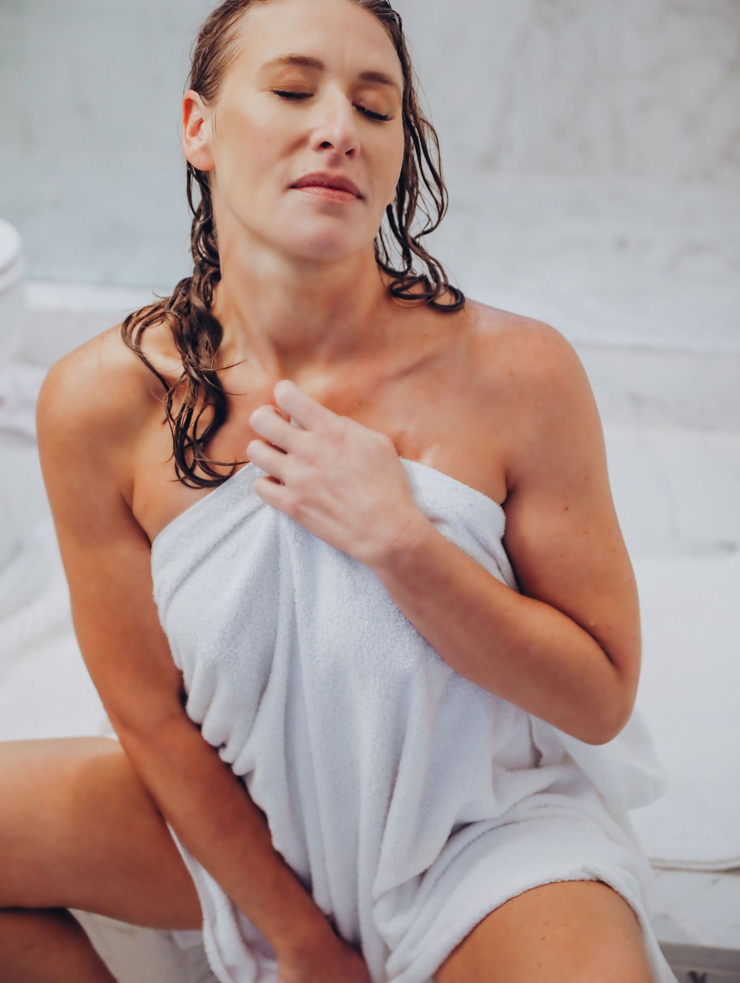Woman posing on ground, wet after shower, posing seductively with white towel in marble bathroom for Boudoir by Bri in Saint Louis
