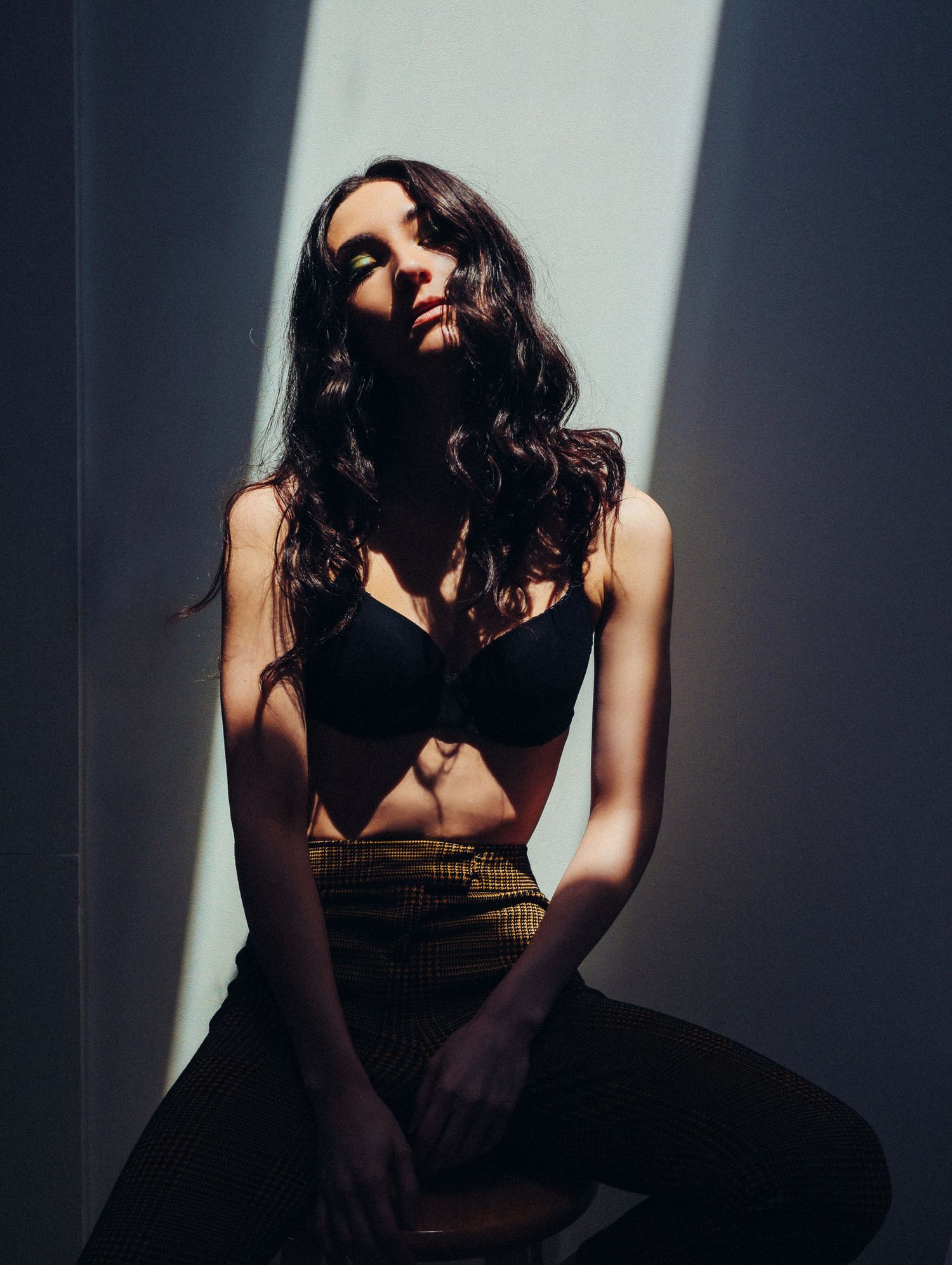 Woman posing in dramatic slice of shadow in black bra and yellow and black plaid pants with long black hair Boudoir by Bri Saint Louis shoot