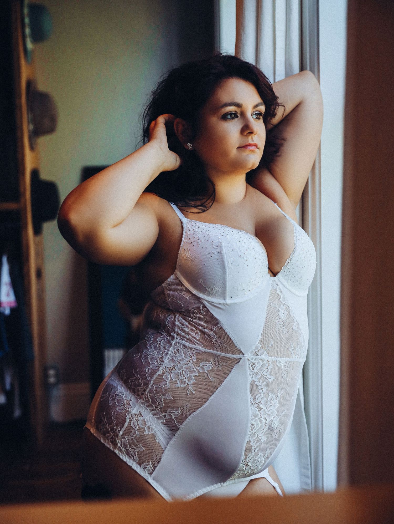 Boudoir portrait of confident and beautiful woman in white bridal lingerie by window for photoshoot with Boudoir by Bri Saint Louis