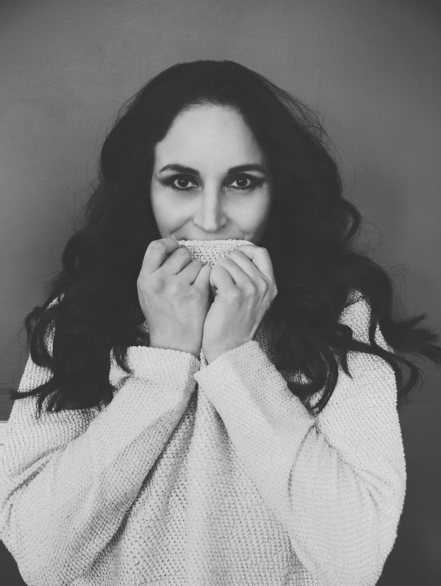 Black and white portrait of beautiful dark-haired woman holding cozy sweater up by face for photoshoot with Boudoir by Bri in Saint Louis
